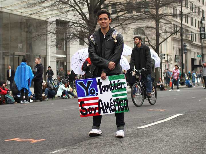 A young man holds a sign saying “Yo, tambien, soy American” which translates to “I am also American.”